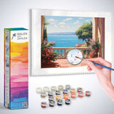 Malen nach Zahlen - Mediterranes Flüstern, Terrasse, hand mit Pinsel, pastellfarbene Blumentöpfe, Aussicht auf azurblaues Meer und Segelboote.