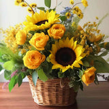 Leuchtender Blumenstrauß mit Sonnenblumen und gelben Rosen in rustikalem Weidenkorb auf Holzoberfläche