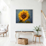 Painting titled 'Sonnentanz' of a sunflower with vibrant yellow petals on a blue background displayed in a bright, airy living room.