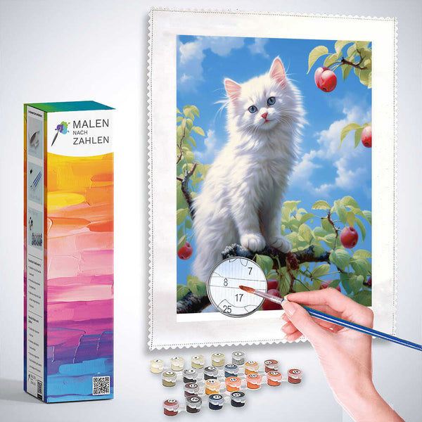 Painting kit featuring a white kitten with blue eyes sitting on a tree branch, surrounded by red apples and a bright blue sky.