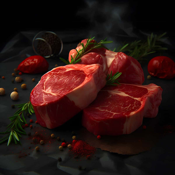 Raw steaks surrounded by herbs and spices on dark surface