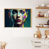 Framed abstract painting of a woman's face with colorful paint splatters hanging on a kitchen wall